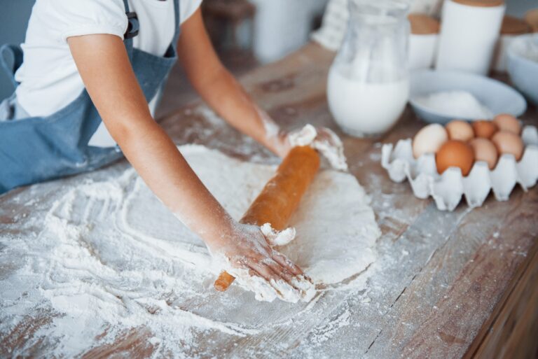 Close up view. Cute kid in white chef uniform preparing food on the kitchen