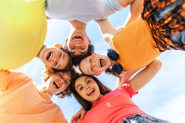 Several smiling teenagers smiling and looking down at camera, hugging